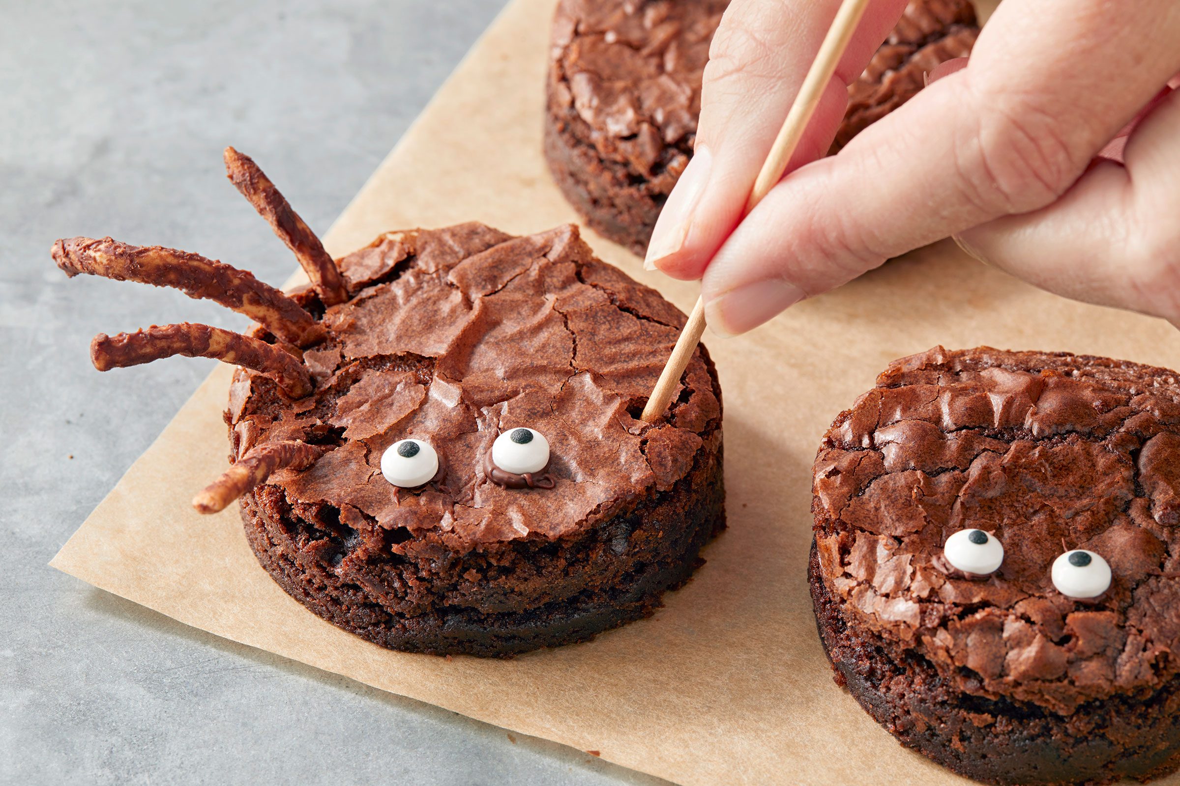 Poking holes in round brownie and adding chocolate coated noodle legs