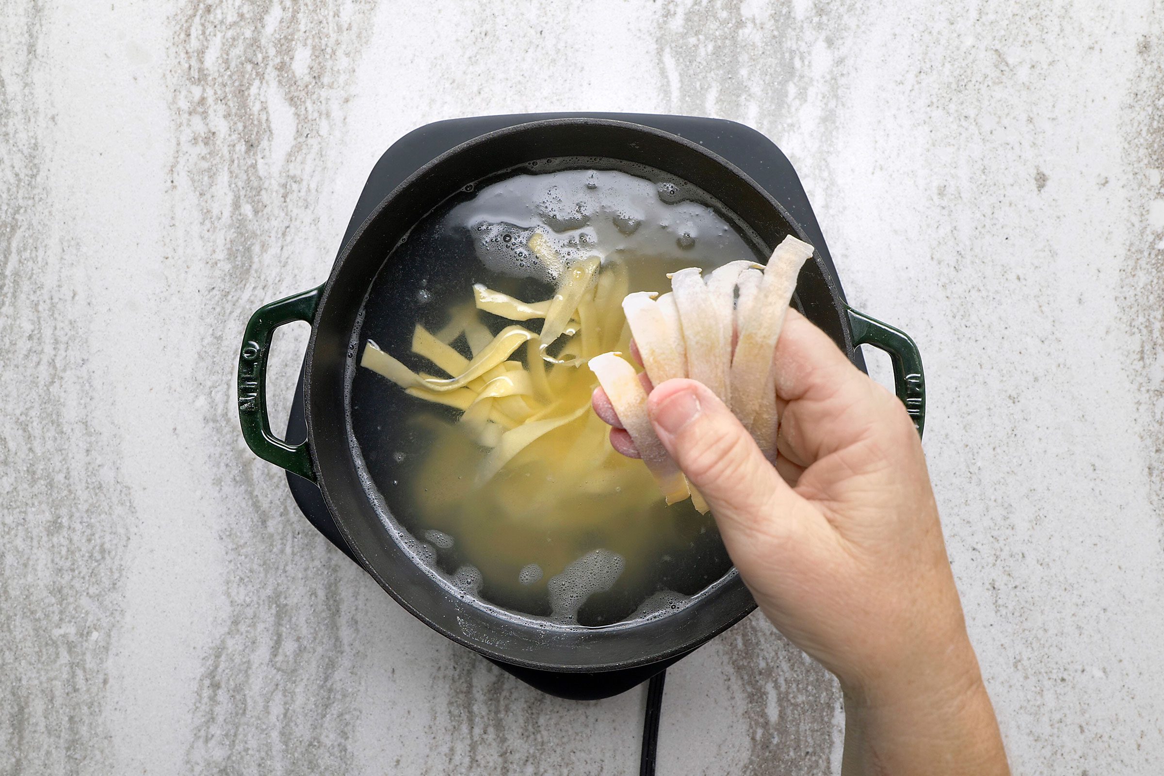 Putting handmade noodles in boiling water in a large pot 