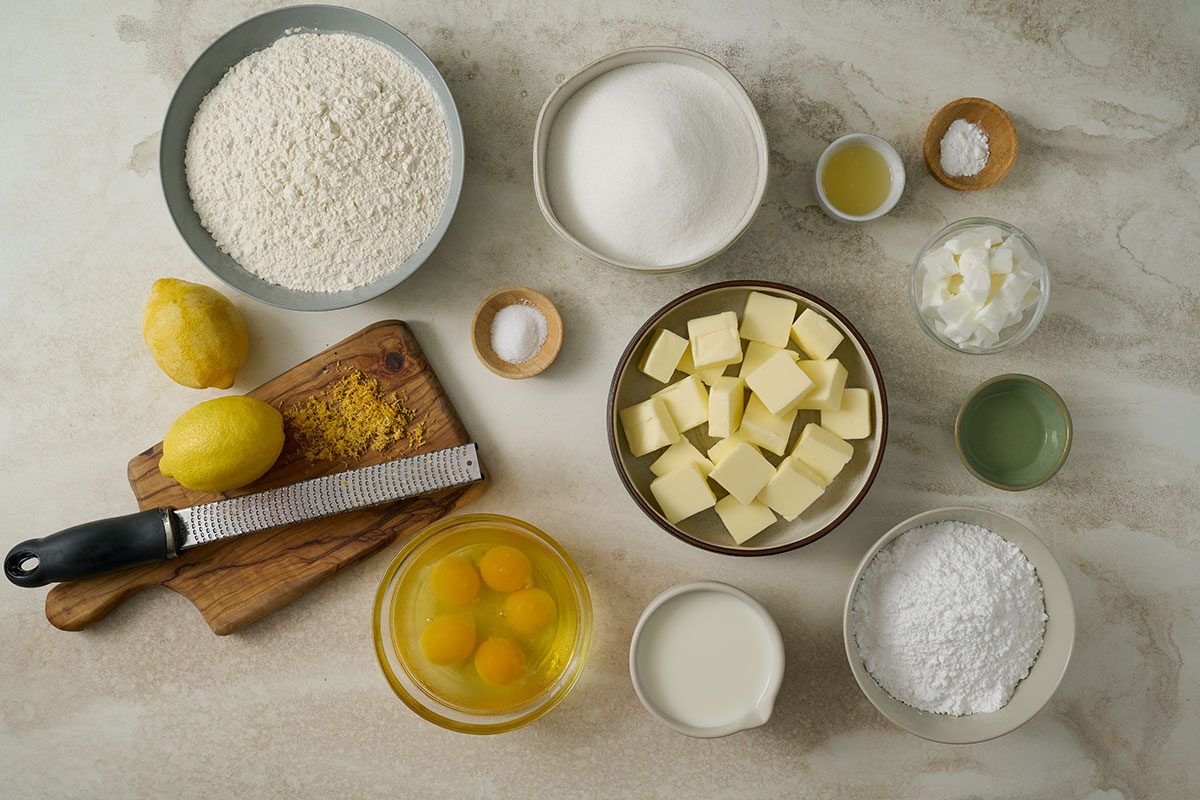 Overhead view of all ingredients for the Taste of Home Lemon Pound Cake recipe, including butter, shortening, sugar, eggs, lemon zest, lemon juice, lemon extract, all-purpose flour, baking powder, salt, whole milk, and ingredients for the frosting (butter, confectioners’ sugar, lemon juice, and lemon zest), arranged neatly on a countertop.