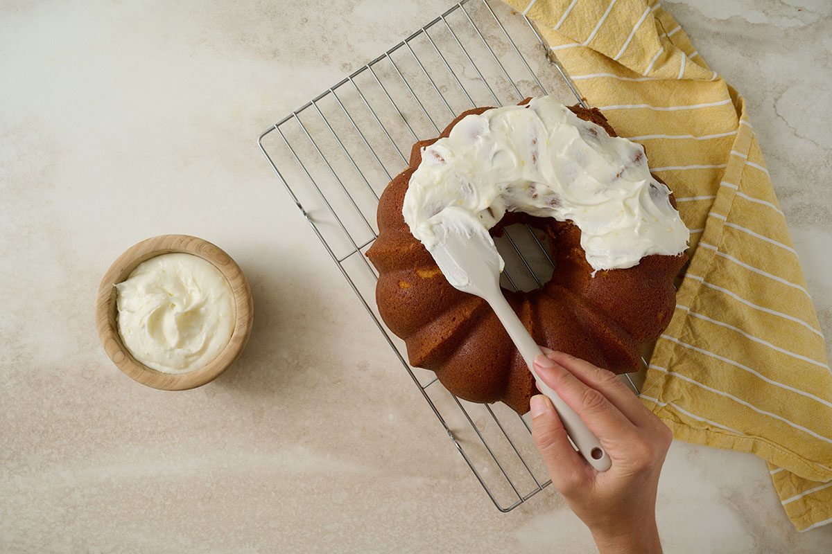 Overhead view of lemon frosting being spread over the cooled Taste of Home Lemon Pound Cake, which rests on a wire cooling rack.