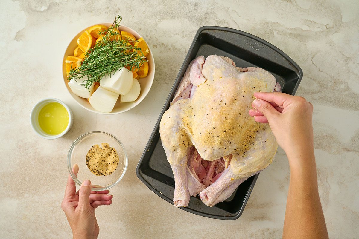 Overhead view of the turkey being patted dry and seasoned with garlic powder, salt, and pepper on the outside for the Taste of Home Orange Turkey recipe.
