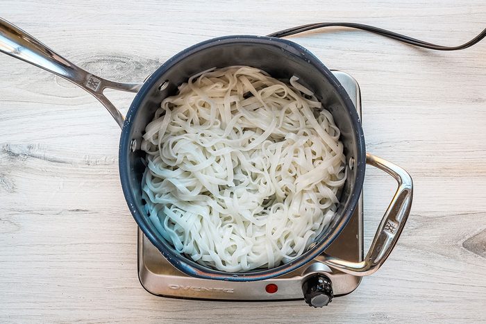 Peanut chicken stir-fry preparation: rice noodles cooked in the pan.
