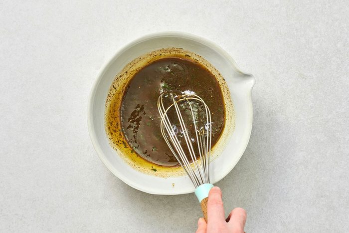 Whisking olive oil, vinegar, pesto, salt, and pepper in a small bowl