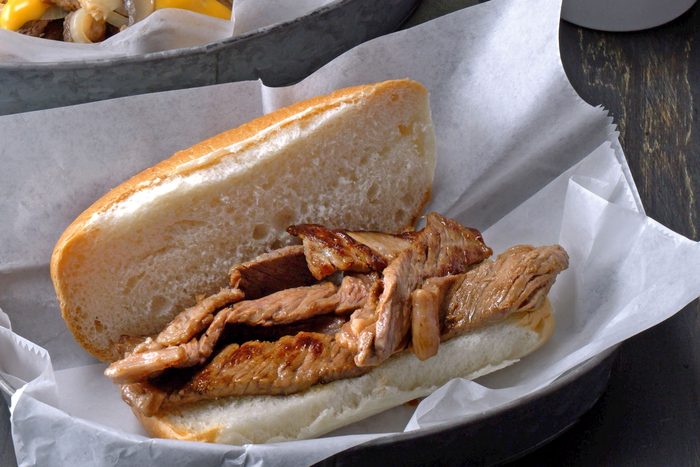 Assembling philly cheesesteak in sliced roll by adding browned ribeye steak