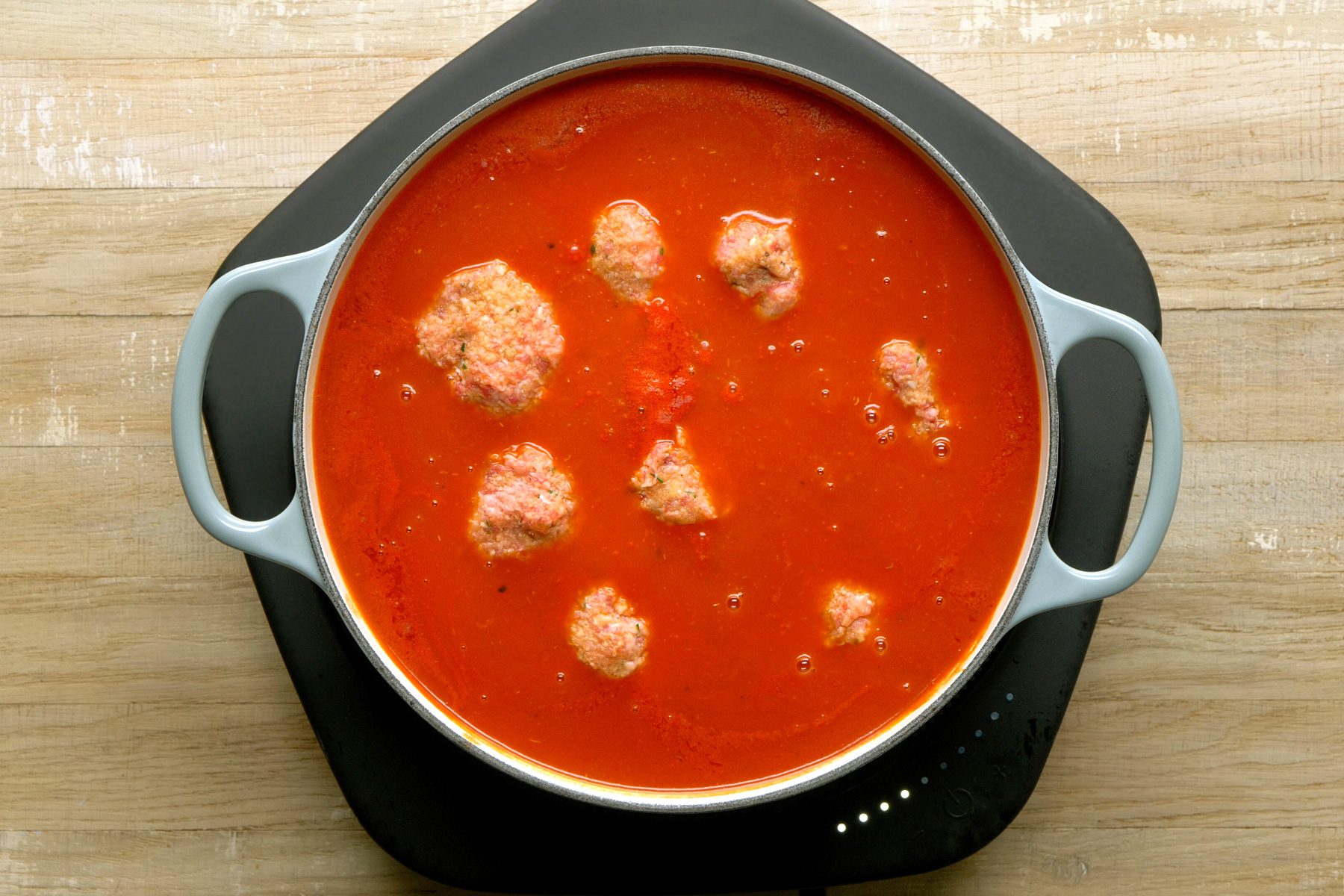 Adding raw meatballs to the simmering sauce.
