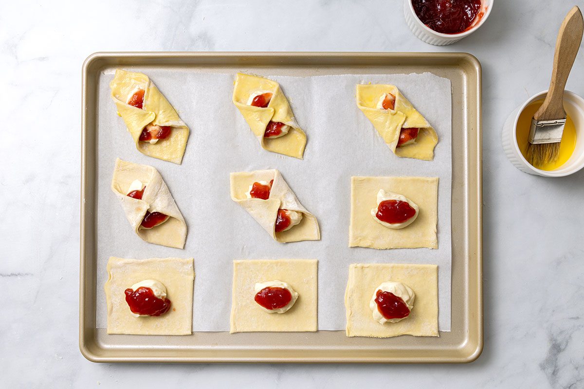 1 tablespoon of the cream cheese mixture in the center of each pastry square, topped with a teaspoon of jam on a baking sheet for step three of Puff Pastry Danish recipe for Taste of Home