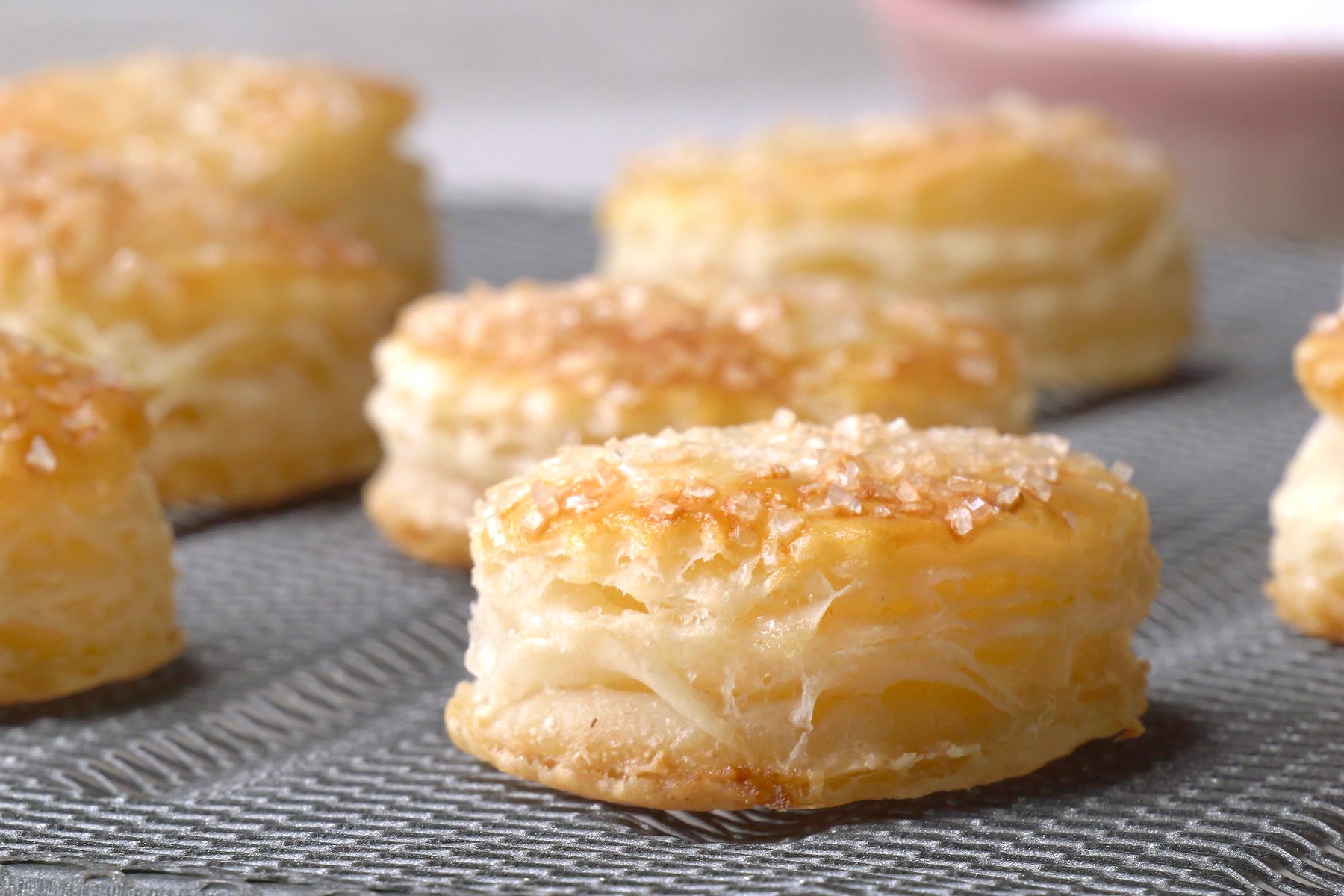 closeup shot of a baking rack filled with golden-Puff pastries sprinkled with sugar crystals, a bowl of sugar crystals sits beside the rack