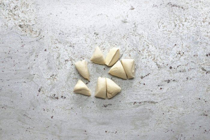 Dough being sliced into small pieces on a marble surface.