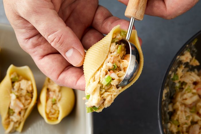 Seafood mixture being added to boiled pasta shells