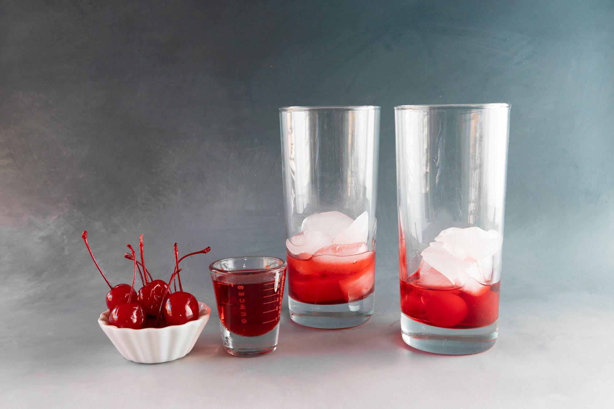 Drop two maraschino cherries into the bottom of the glass, then fill it halfway with ice cubes and pour 1 ounce of grenadine syrup
