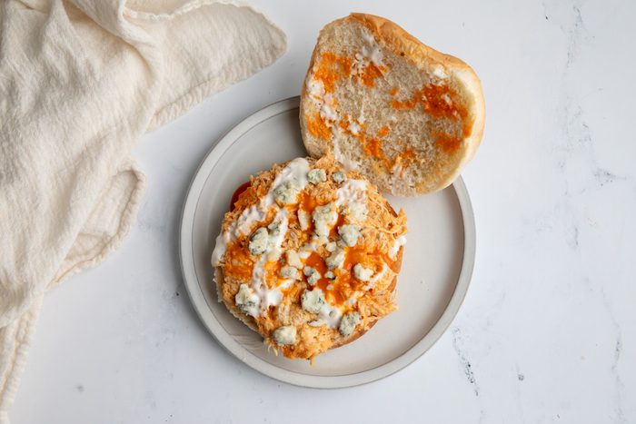 Close up shot for Taste of Home Shredded Buffalo Chicken with mixture on a bun dressed with blue cheese and ranch dressing.