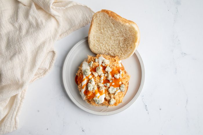 Beauty shot for Taste of Home Shredded Buffalo Chicken with mixture on a bun dressed with blue cheese and ranch dressing.