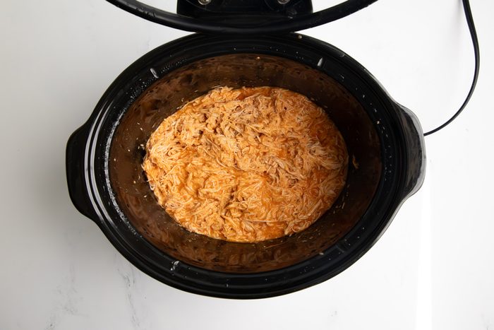 Overhead shot for Taste of Home Shredded Buffalo Chicken with chicken, buffalo sauce, and ranch seasoning in a large slow cooker after being shredded.