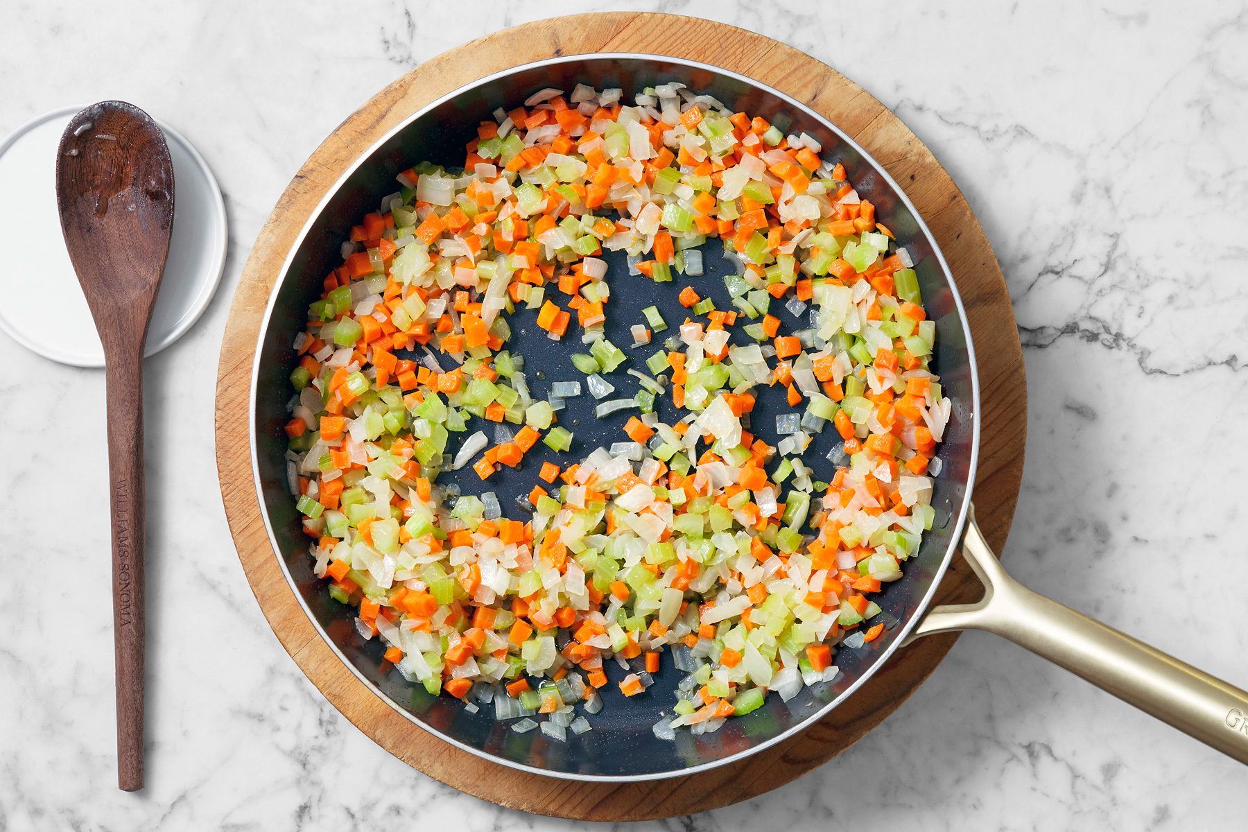 Overhead shot of the same skillet; cook and stir onions; carrots; celery in remaining oil until tender 5-7 minutes; add garlic and cook 1 minute longer; spoon; marble surface.