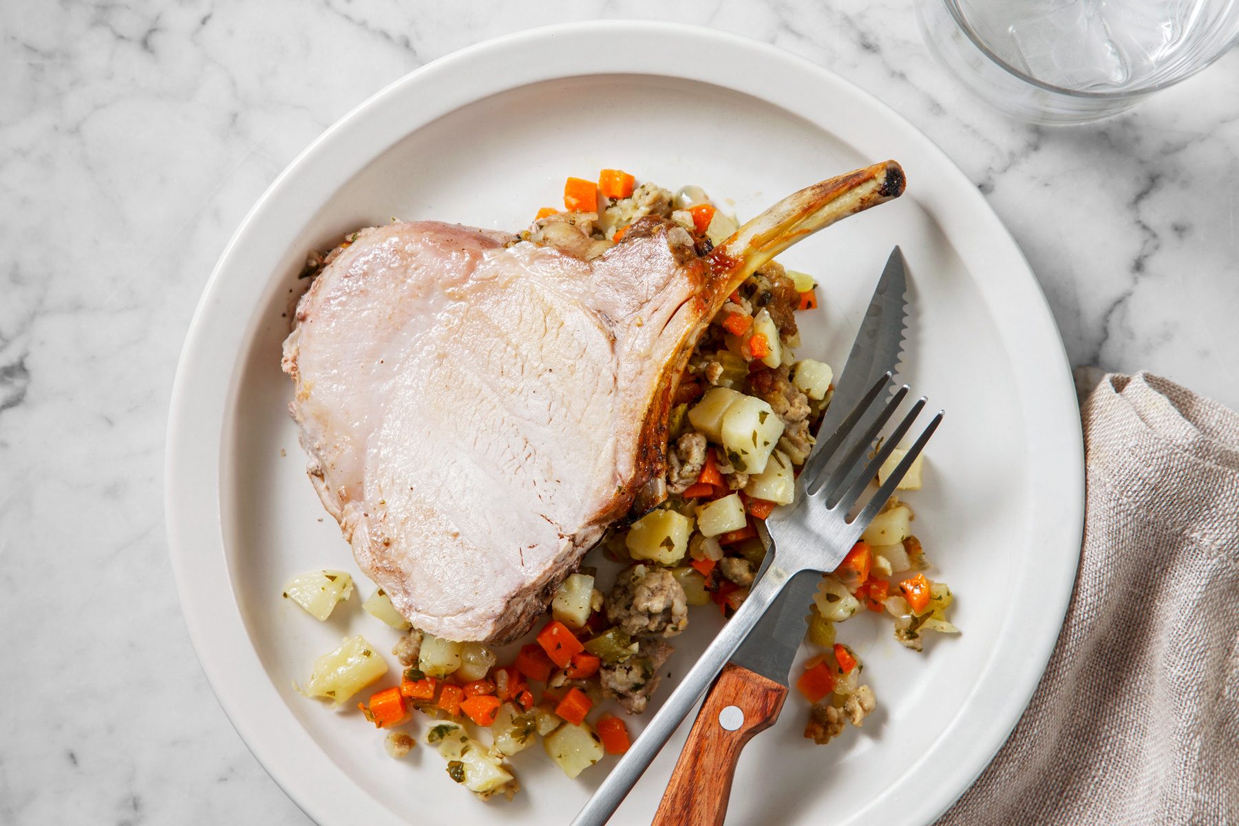 Overhead shot of Crown Roast of Pork with Stuffing; thicken pan juices and serve with stuffing and pork on plate; knife and fork; napkin; a glass of water.