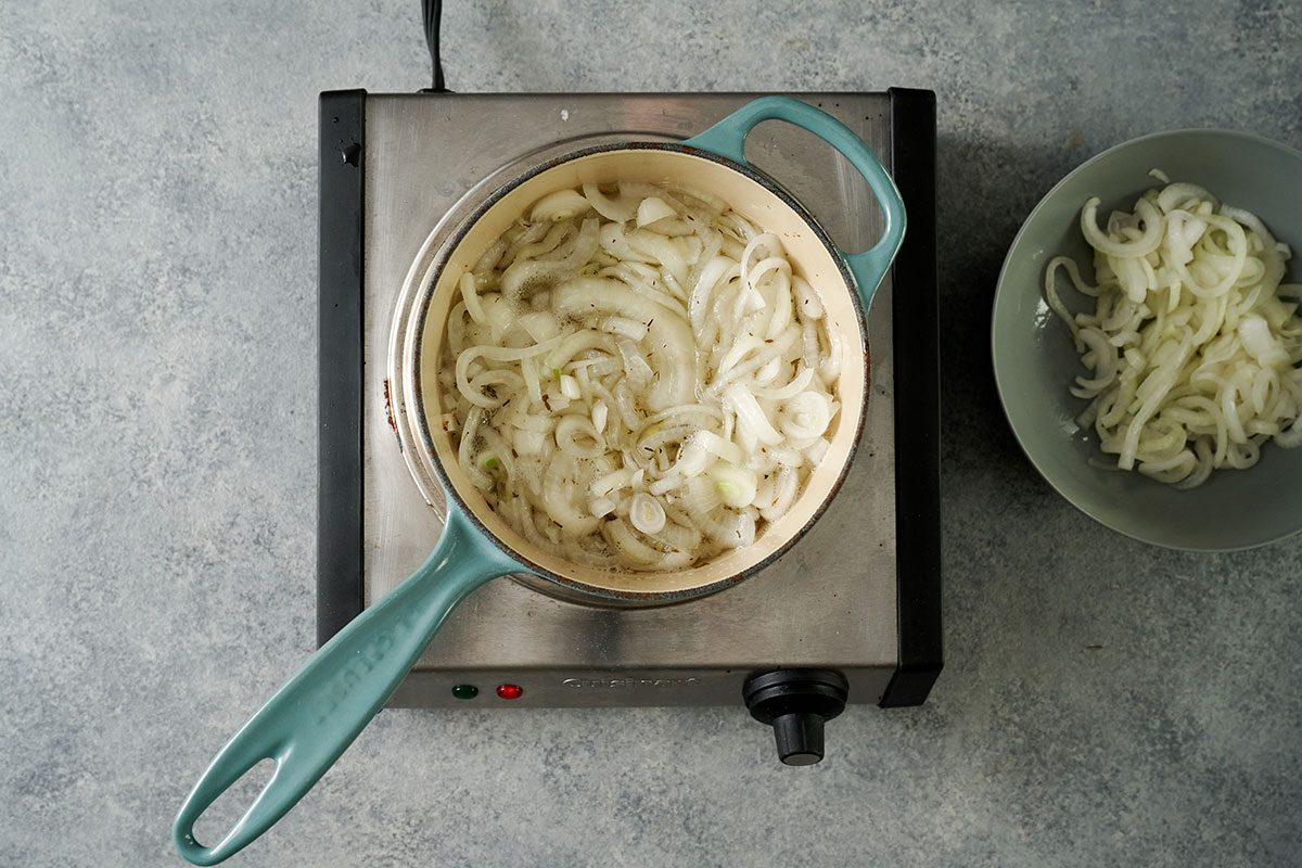 Overhead view of vinegar, sugar, and dried thyme boiling in a Dutch oven, with onions being added to simmer for the Taste of Home Pickled Sweet Onions recipe.