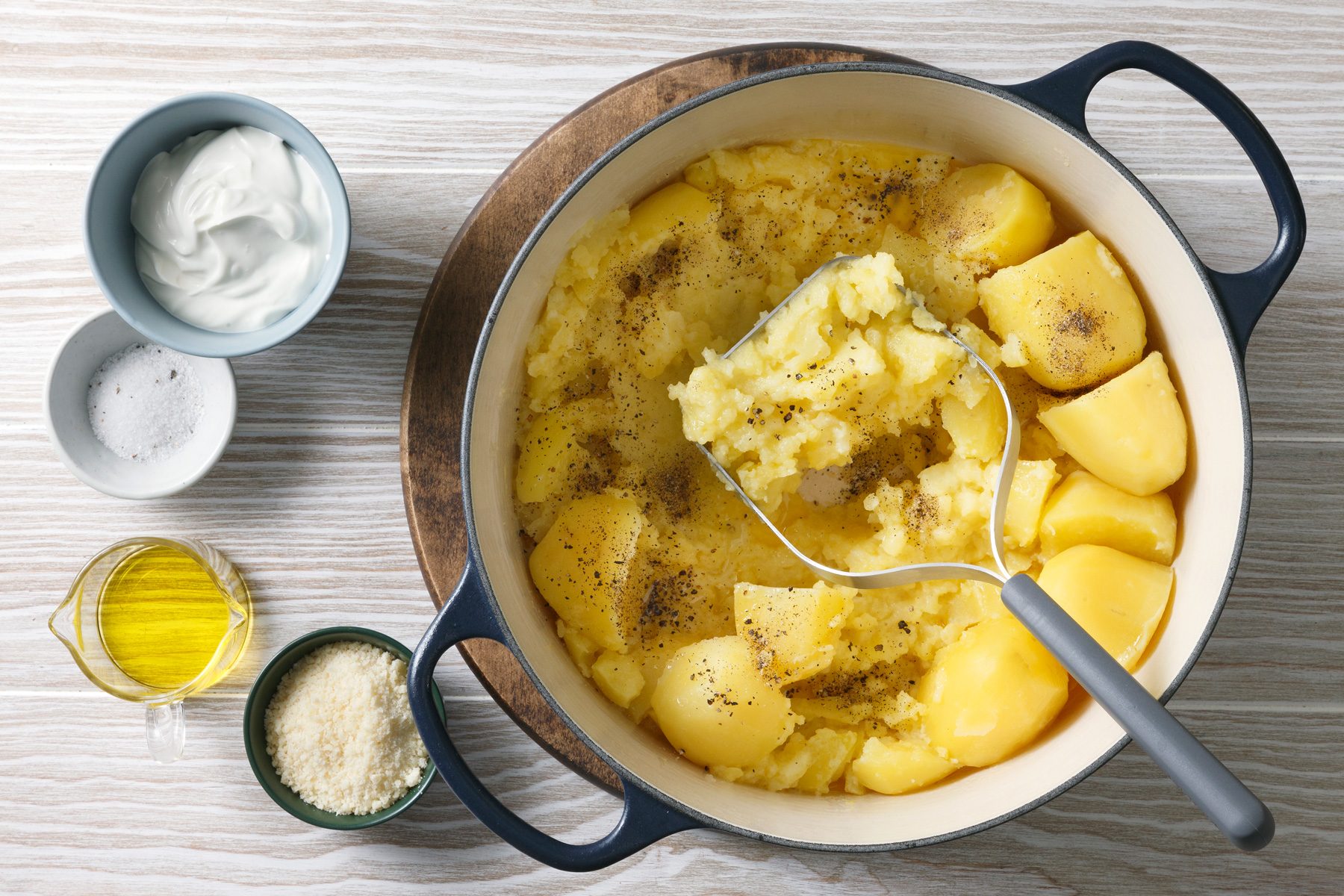 Overhead shot of gently mash potatoes while gradually adding milk and butter mixture; sour cream; Parmesan and truffle oil to reach desired consistency; wooden surface;