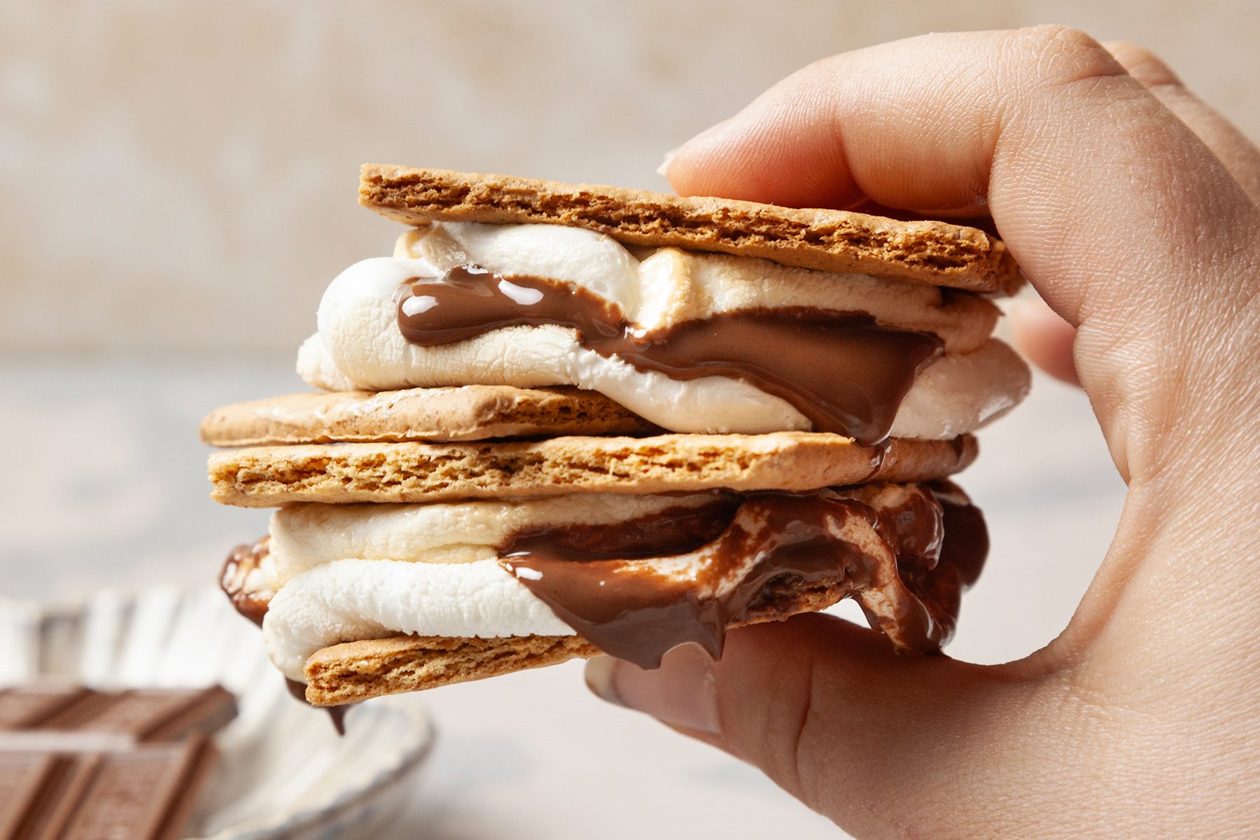 A hand holds a s'more with melted chocolate and marshmallow between graham crackers.