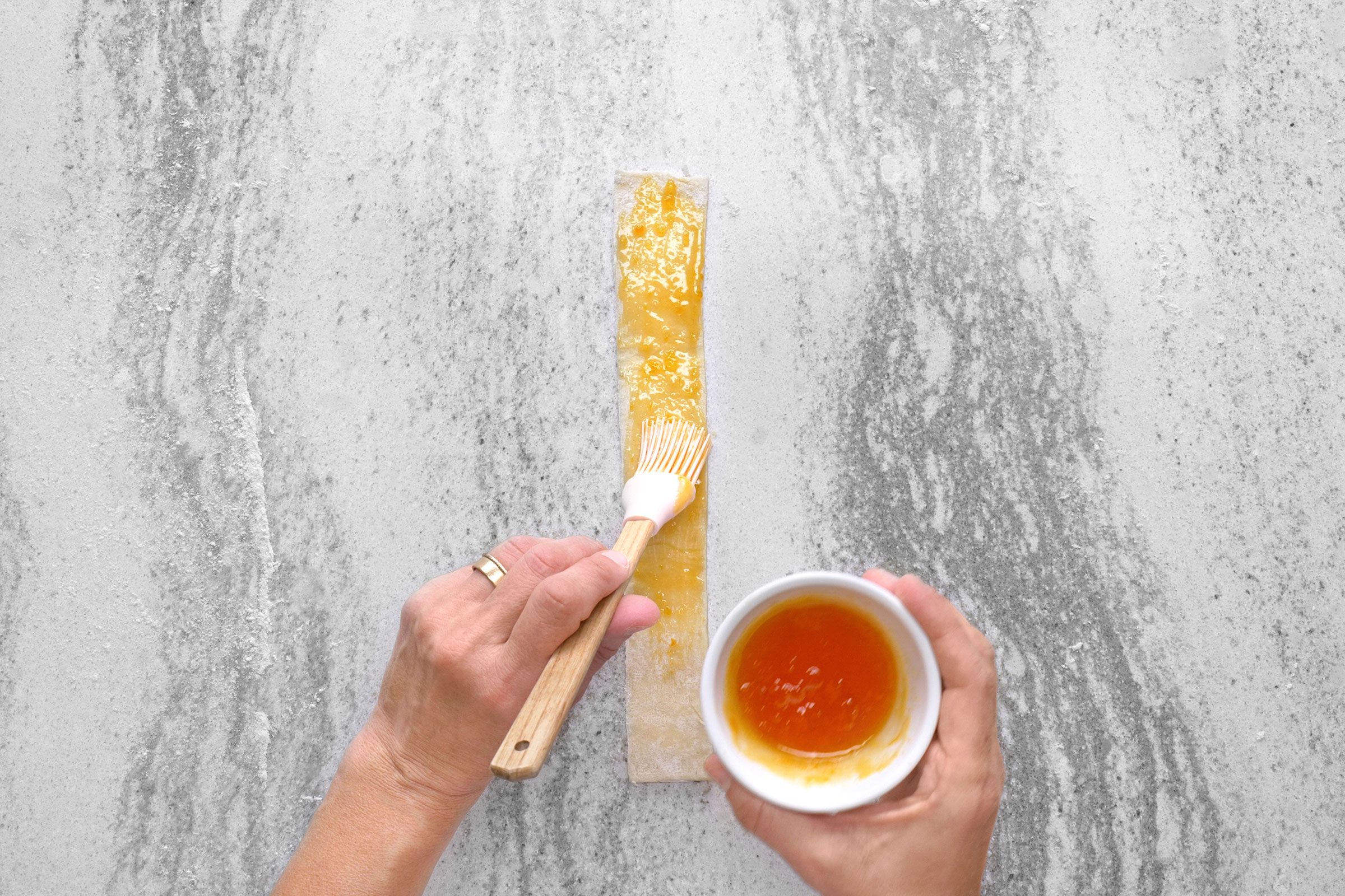 Brushing apricot preserves on puff pastry strips using a brush