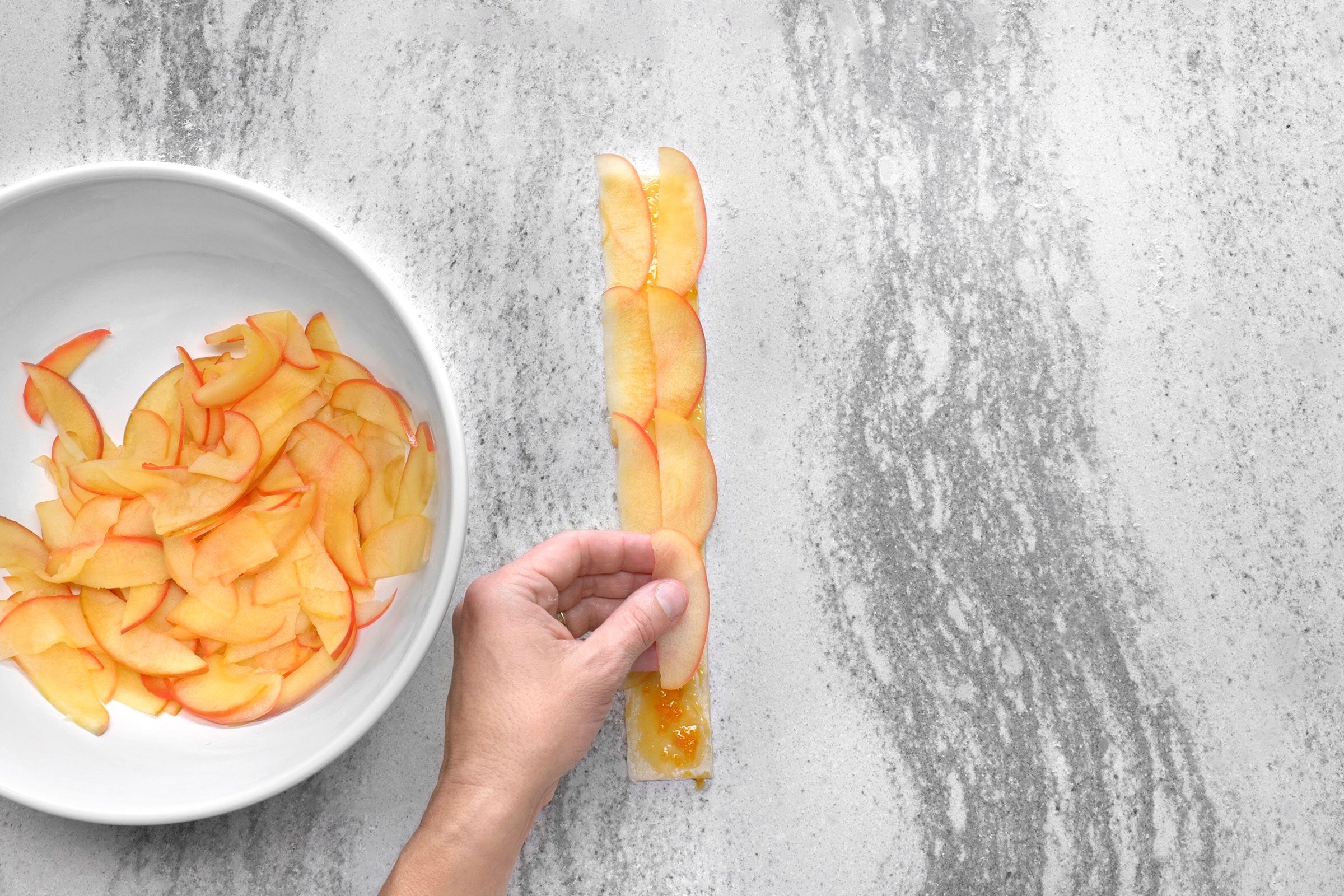 Arranged apple slices on top of each other forming a straight strip on puff pastry strip