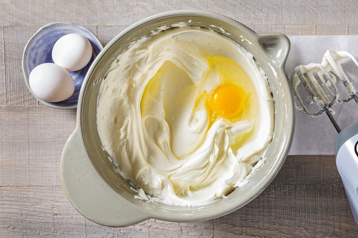 Cream cheese, sugar and eggs in a large bowl mixed together with two whole eggs on the side