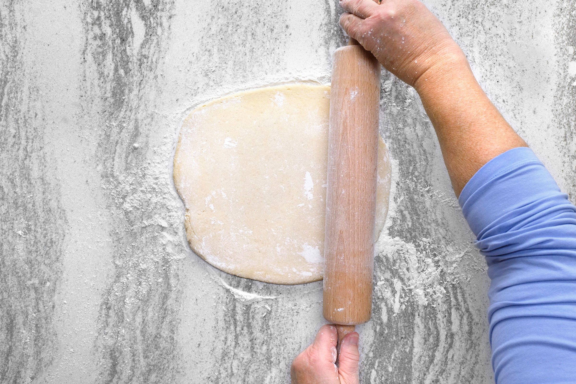 Rolling cookie dough into a thin sheet using a rolling pin on kitchen countertop