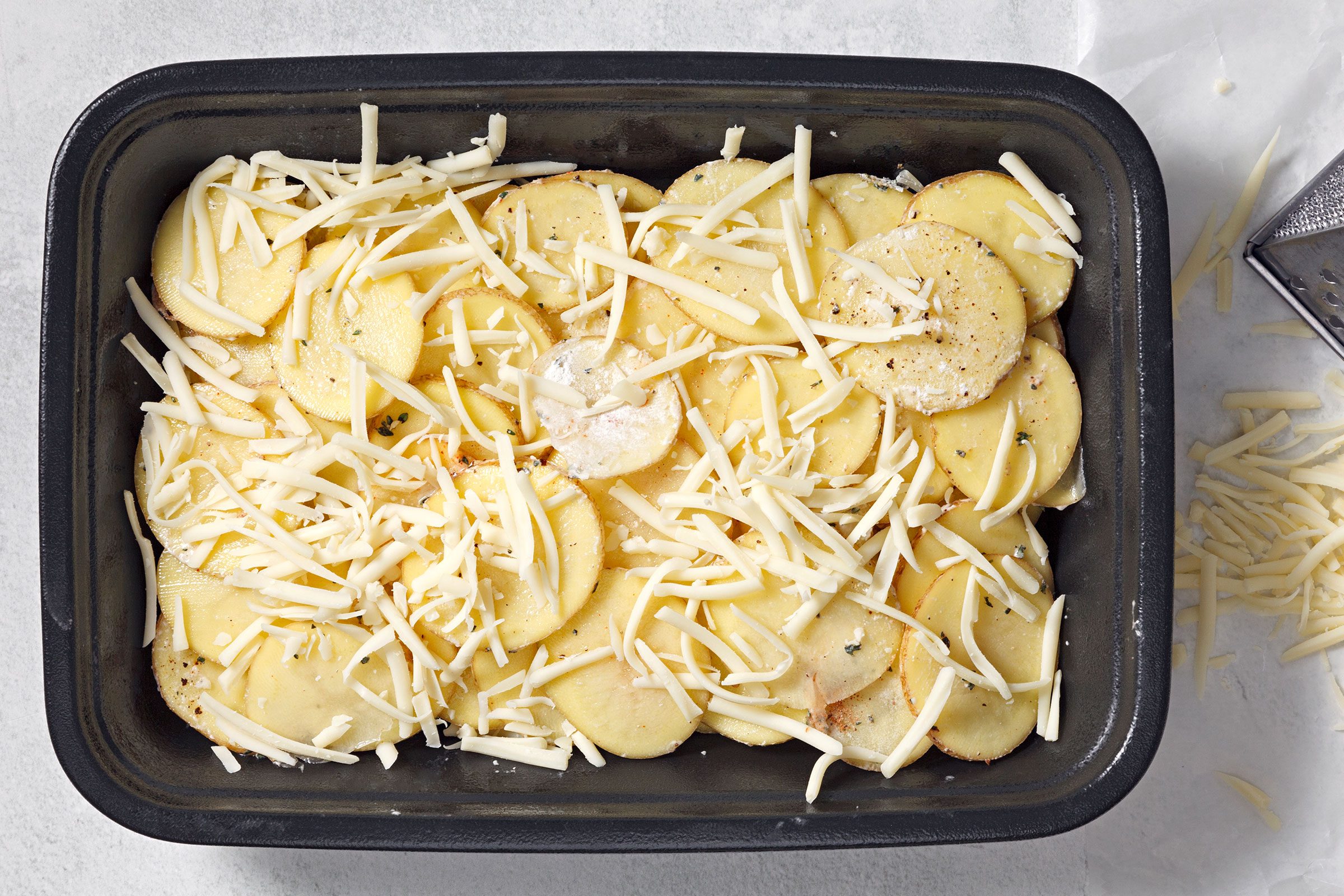 Grated Gruyere cheese spread on seasoned potatoes layer in a baking dish