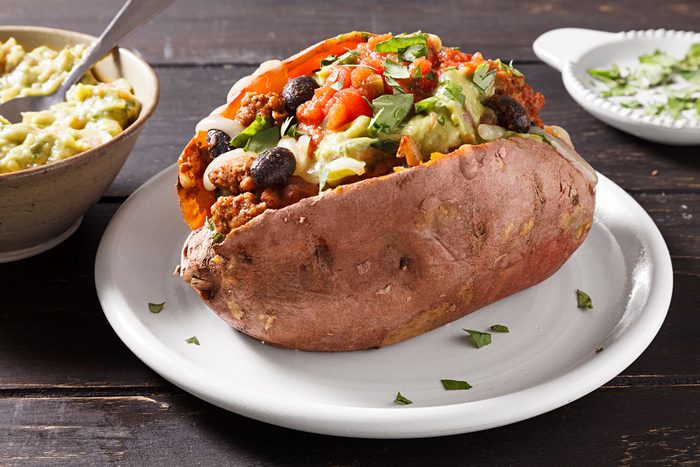 Stuffed Sweet Potatoes served in a plate with guacamole, salsa and cilantro