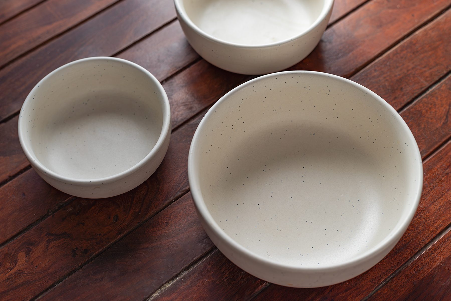Three white ceramic bowls of varying sizes are placed on a wooden surface. The bowls are empty and arranged in a slightly triangular formation, showcasing their simple, minimalist design.