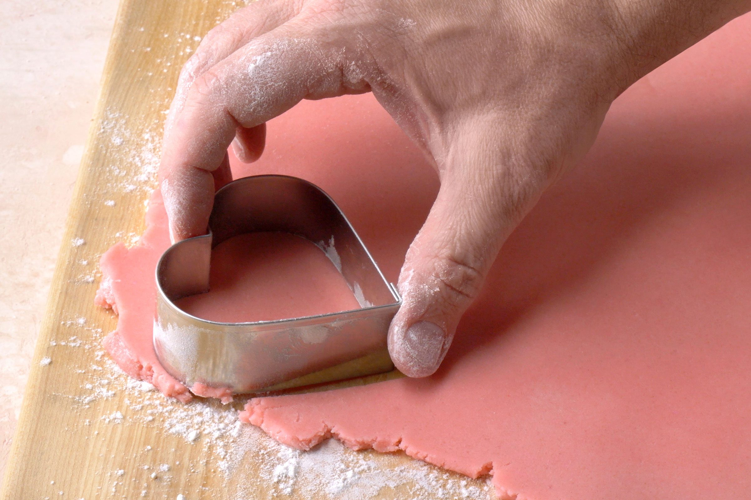 Cutting pink cookie dough sheet with a heart shaped cookie cutter