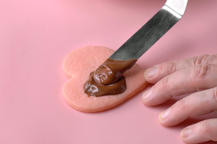 Applying chocolate glaze on pink heart shaped cookie
