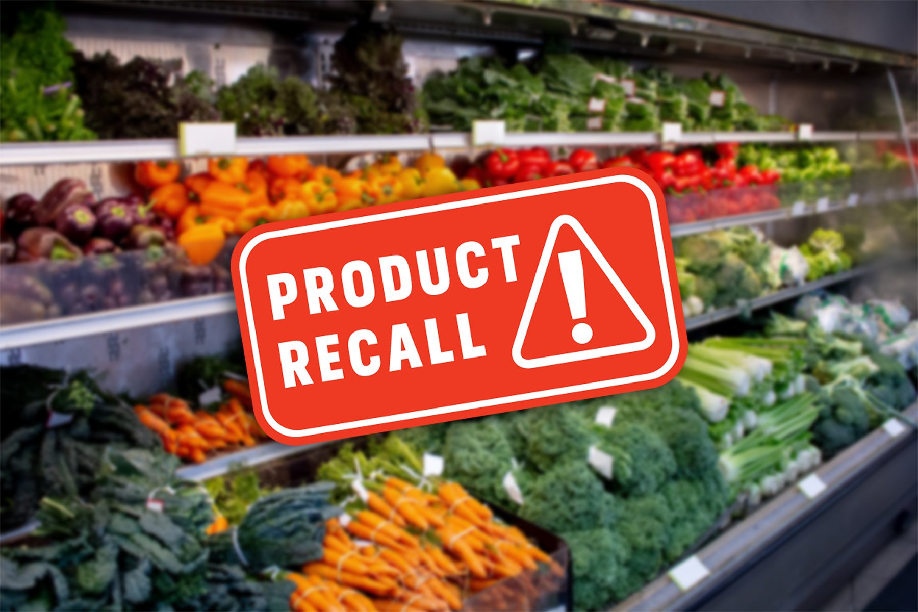 A grocery store display of fresh vegetables, including carrots, broccoli, and leafy greens, with a bold red "Product Recall" sign featuring an exclamation mark superimposed over the image.