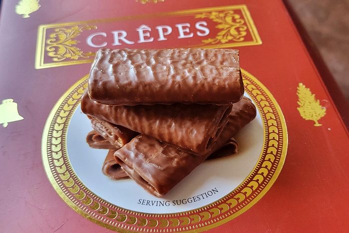 A stack of rectangular chocolate-covered crepe cookies sit on top of a red box with a white circle
