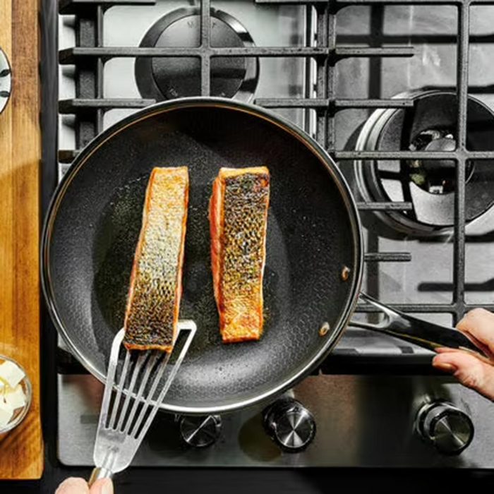 Two pieces of salmon cooking in a black frying pan on a gas stovetop