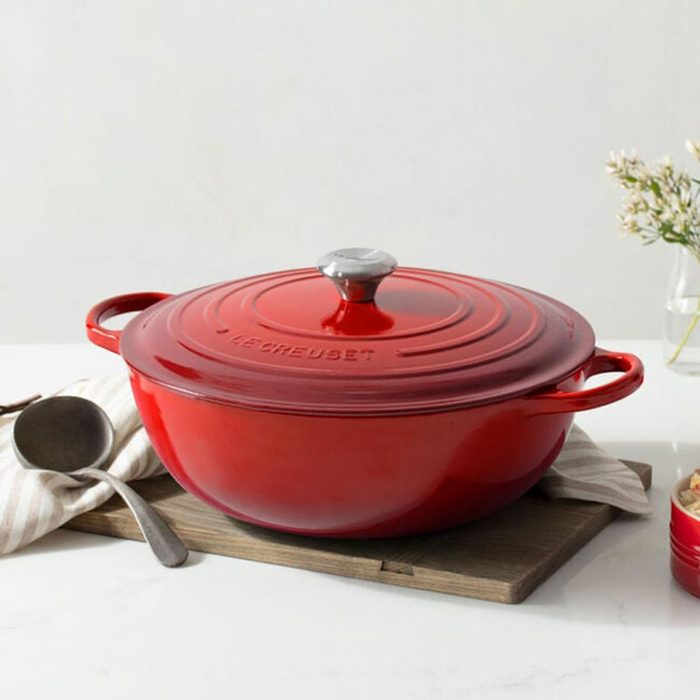 Deep red dutch oven on a stone slab in front of a clean white tile background