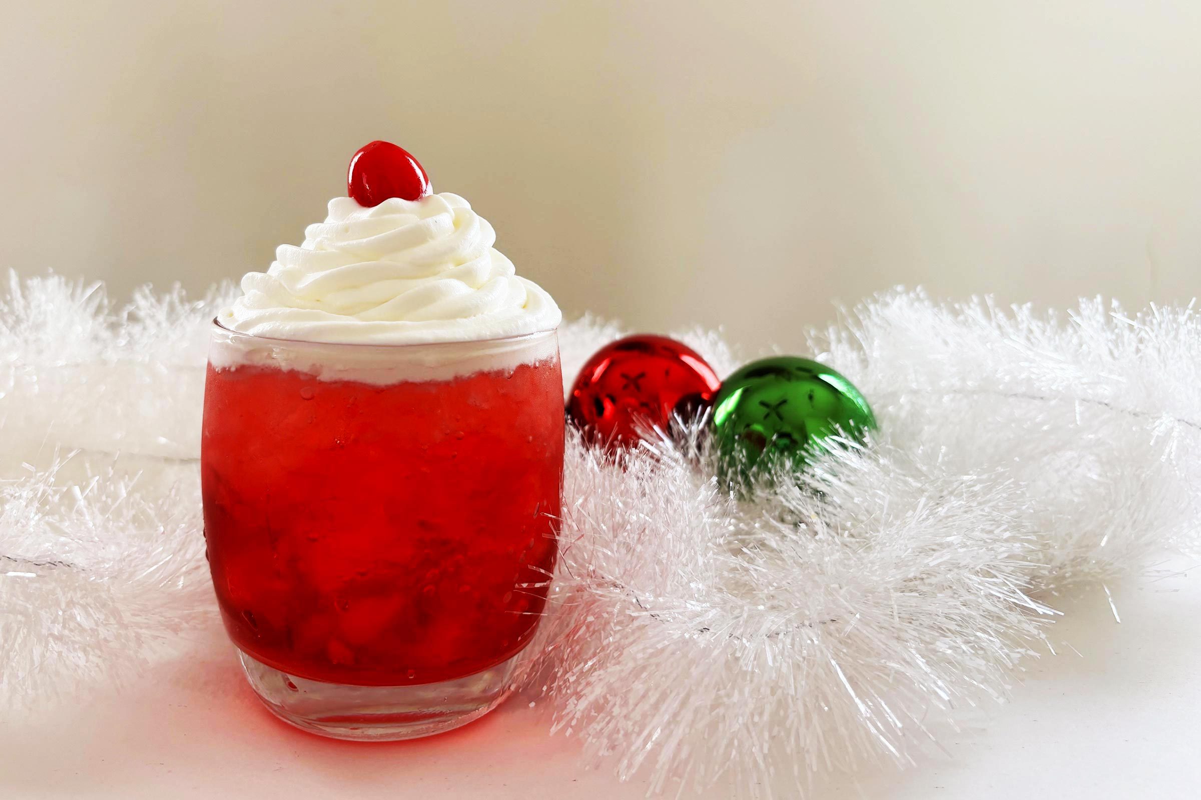 A Santa Hat Shirley Temple Sits in front of a Festive Holiday Background of Tinsel and Red and Green Ornaments
