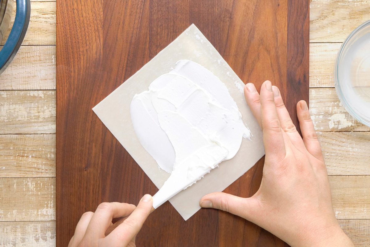 cream cheese being spread on egg roll wrapper