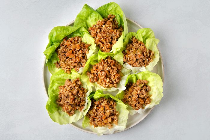 A plate of lettuce wraps filled with a mixture of cooked brown rice, chopped vegetables, and minced meat. The vibrant green lettuce contrasts with the earthy tones of the filling, all arranged neatly on a white plate.