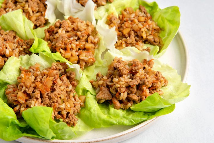 Lettuce wraps filled with a mixture of minced meat, brown rice, and diced vegetables, arranged on a round white plate. The dish is set against a light background.