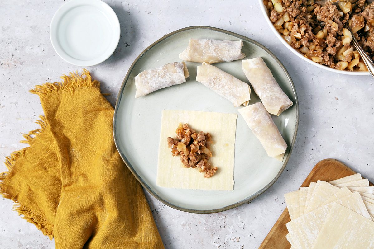 wanton wrapper with two tablespoons of filling in the centre next to more paper covered wrappers
