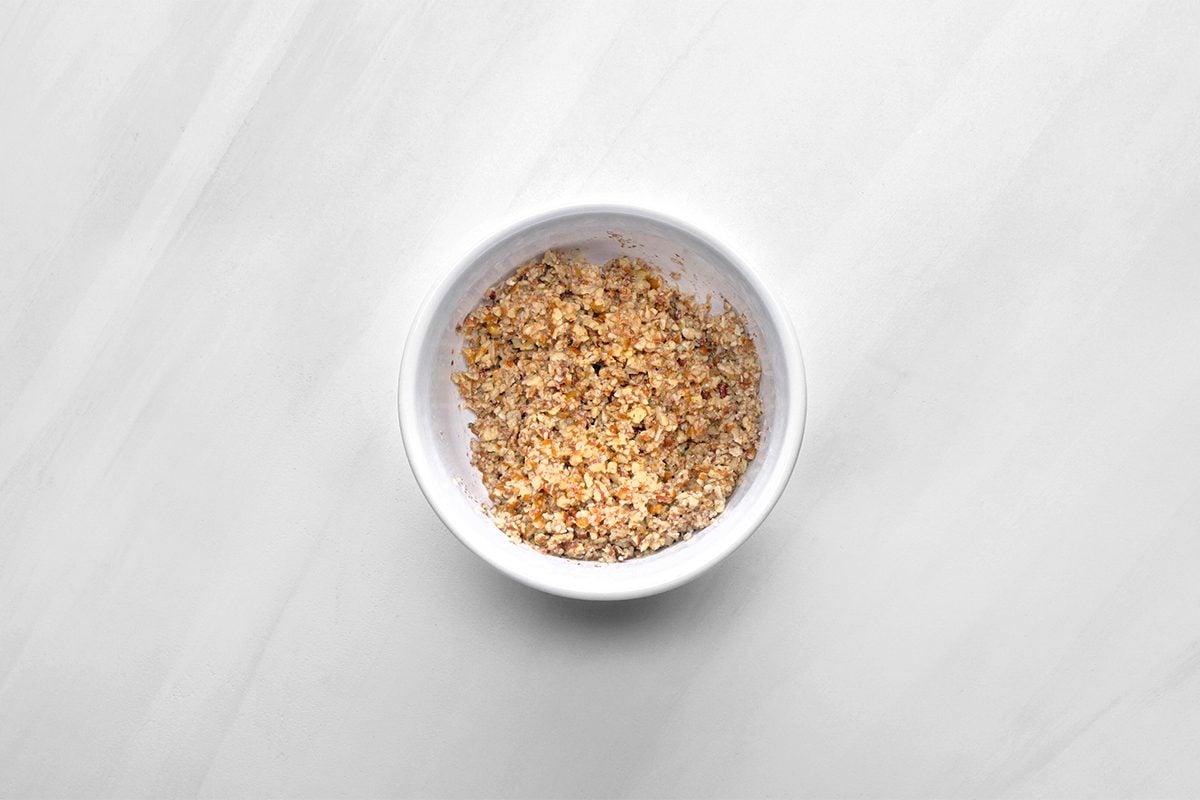 A small white bowl filled with granola, placed on a light gray surface.
