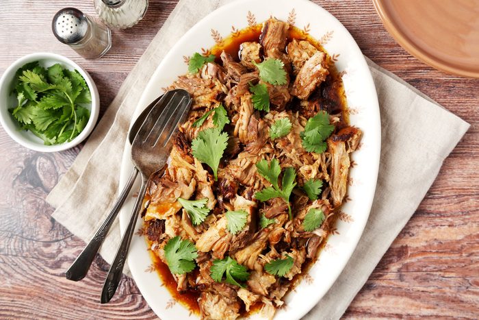 Char Siu Pork shot on a wooden surface. Shredded pork served on a platter with cilantro for garnish; overhead
