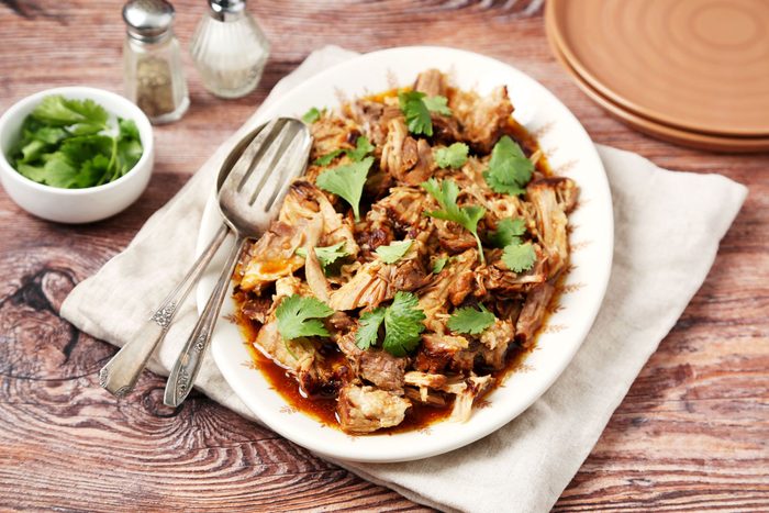 Char Siu Pork shot on a wooden surface. Shredded pork served on a platter with cilantro for garnish; 3/4th