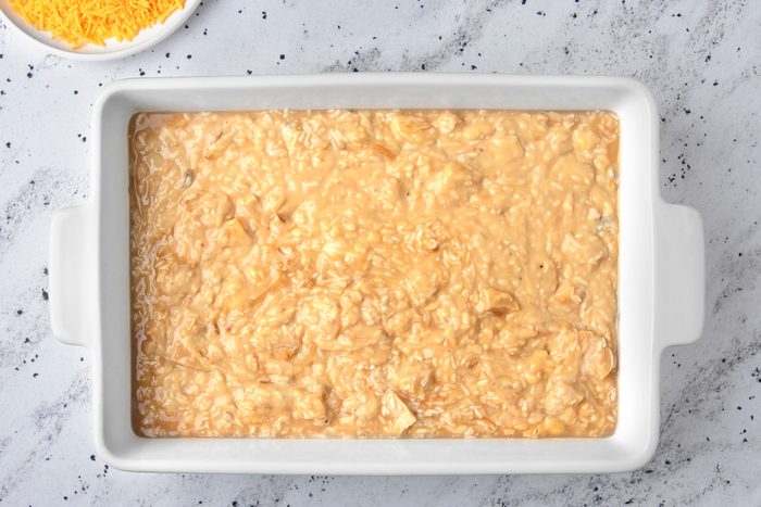 overhead shot of a white rectangular baking dish filled with a mixture of cooked rice, chicken, and a creamy sauce; the dish is sitting on a light gray speckled countertop