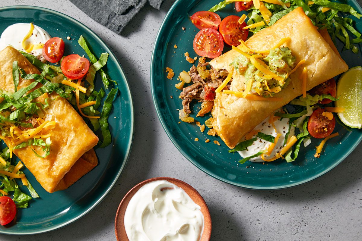 Overhead shot of Chimichangas; Serve on round plates with toppings of your choice; napkin; grey marble surface;