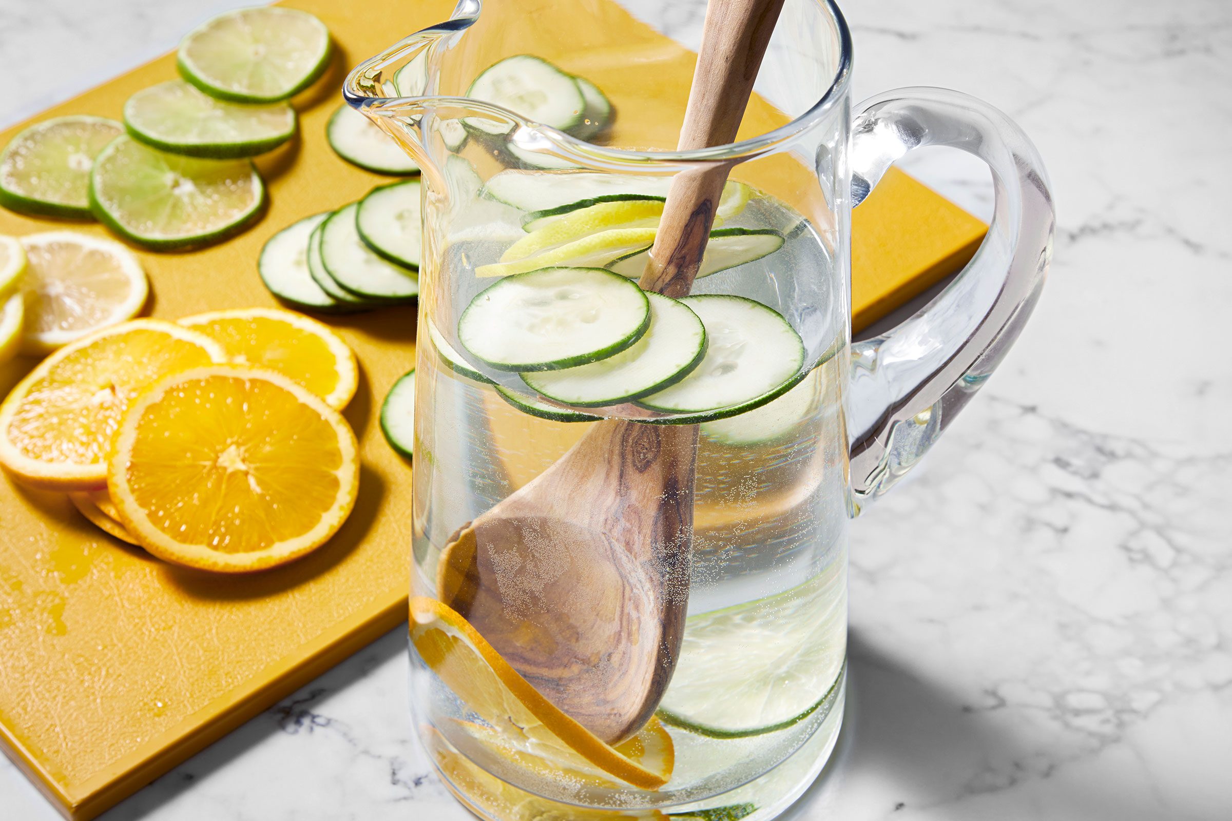 Cucumber Water in a jar with wooden ladle along with sliced lemons, cucumbers and orange