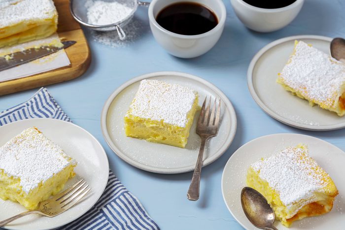 Four custard cakes served on individual white plates, dusted generously with powdered sugar