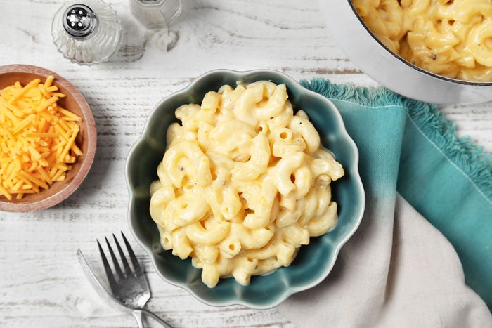 A plate of macaroni and cheese with a blue and white bowl and napkin on a white table
