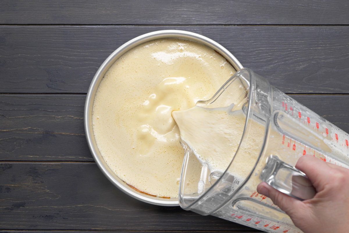 milk, eggs, vanilla and salt blended mixture being added to cake pan lined with caramel