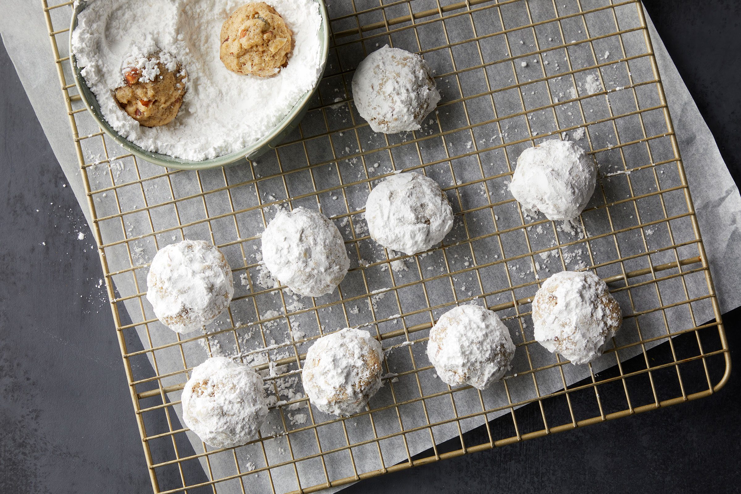 Rolling baked cookies in confectioners' sugar and placing on wire racks